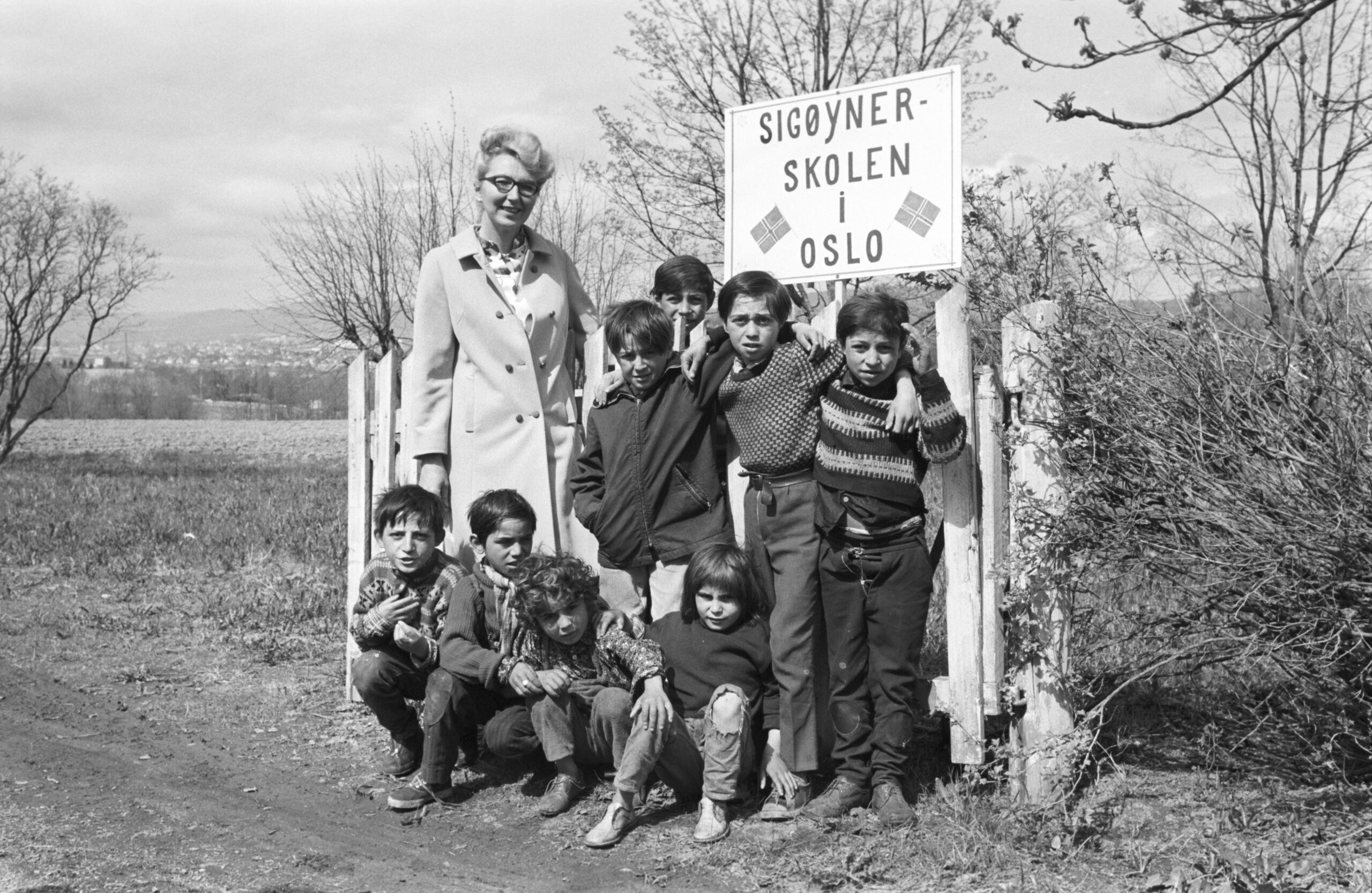 L&aelig;rer sammen med elever foran et skoleskilt