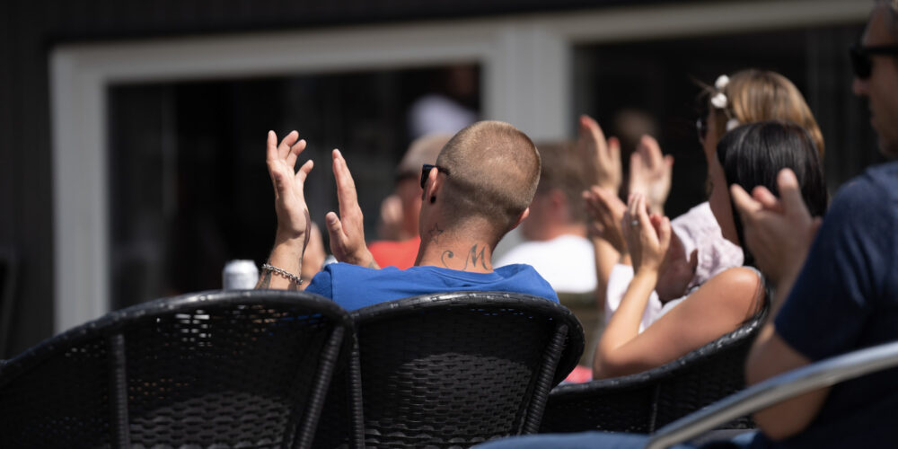 Publikum som sitter p&aring; stoler utend&oslash;rs og klapper